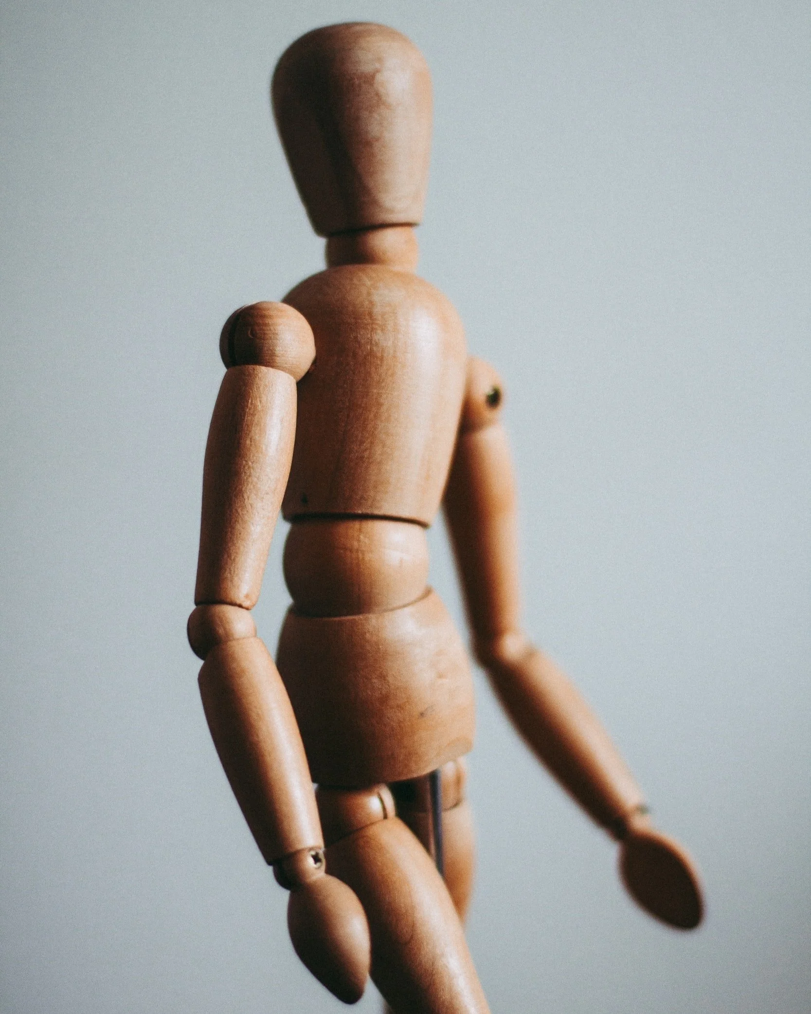 A wooden anatomical artist figure posed against a soft grey backdrop